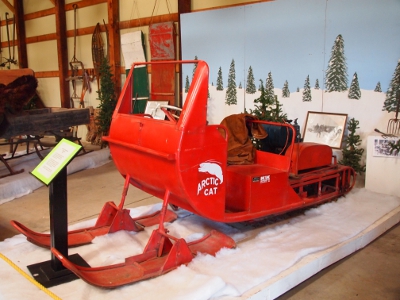 [Large red sleigh with two large skies on the front and a conveyor belt like tread in the back. This snowmobile could seat two people side-by-side.]